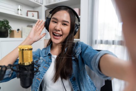 Photo for Host channel young beautiful Asian girl making selfie with smartphone wearing headphones at modern studio home office concept of behind the scene broadcaster live streaming on social media. Stratagem. - Royalty Free Image