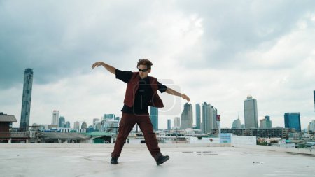 Photo for Motion shot of B-boy dance performance by professional street dancer at rooftop with sky scrapper, city view. Attractive asian hipster show energetic footstep. Outdoor sport 2024. Endeavor. - Royalty Free Image