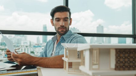 Photo for Portrait of smart skilled engineer checking house model while holding blueprint. Professional businessman choosing project while looking at architect model and thinking designing,choosing. Disputation - Royalty Free Image