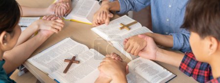 Cropped image of diversity people hand priing together at wooden church on bible book while hold hand together with believe. Concept d'espoir, de religion, de foi, de bénédiction divine. Émergence.