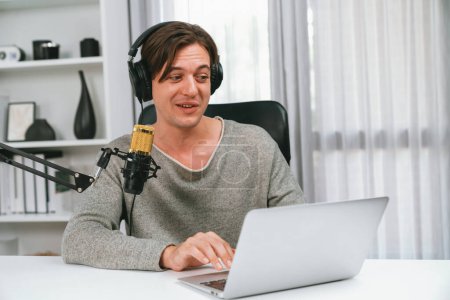 Photo for Host channel in smiling smart broadcaster recording, talking show with script and smartphone on desk on live social media, wearing headphones to record video streamer at modern home studio. Pecuniary. - Royalty Free Image