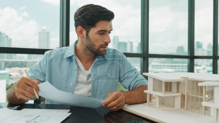 Photo for Portrait of smart skilled engineer checking house model while holding blueprint. Professional businessman choosing project while looking at architect model and thinking designing,choosing. Disputation - Royalty Free Image