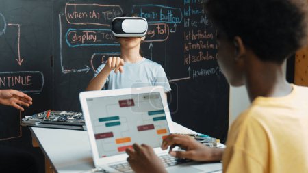 Téléchargez les photos : African boy programing system while caucasian girl enter metaverse while sitting at blackboard with engineering code written.Highschool girl wearing VR or headset in STEM technology. Édification. - en image libre de droit