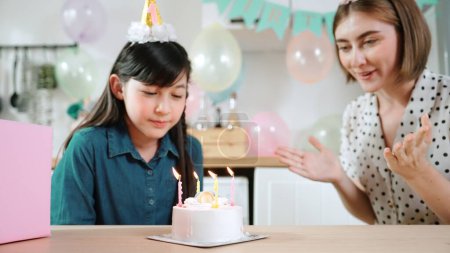Energetische Tochter und Mutter singen Geburtstagslied, während sie gemeinsam in die Hände klatschen. Kaukasische Mutter feierte Geburtstag, während mit Kuchen im Esszimmer mit bunten Luftballons dekoriert. Pädagogik.