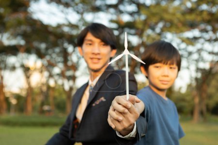 Téléchargez les photos : Garçon asiatique et homme d'affaires tenant le modèle d'éolienne ensemble comme concept du Jour de la Terre en tant qu'entreprise sociale responsable de rendre plus vert avec l'énergie alternative écologique pour la génération future durable. Pneumatique - en image libre de droit