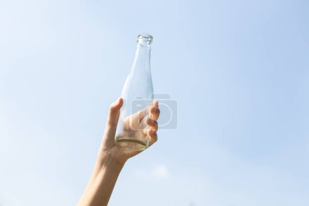 Photo for Recyclable glass bottle held in hand up on sky background. Hand holding plastic waste for recycle reduce and reuse concept to promote clean environment with effective recycling management. Gyre - Royalty Free Image