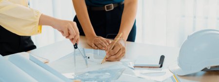 Photo for Professional architect team used divider measure during draft blueprint on table with architectural document, safety helmet and blueprint scatter around. Closeup. Focus on hand. Delineation. - Royalty Free Image