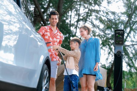 Photo for Outdoor adventure and family vacation camping in nature travel by eco friendly car for sustainable future. Lovely family recharge EV car with EV charging station in campsite. Perpetual - Royalty Free Image