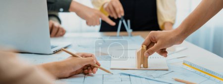 Photo for Professional architect team discussion about architectural project on meeting table with blueprint and wooden block scatter around at modern office. Closeup. Focus on hand. Delineation. - Royalty Free Image