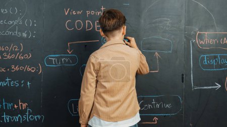 Photo for Back view of smart boy writing engineering prompt on blackboard. Attractive happy student planing a project by using coding and programing system in STEM technology classroom. Closeup. Erudition. - Royalty Free Image