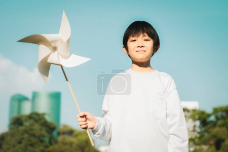 Téléchargez les photos : Petit garçon asiatique tenant un moulin à vent ou un modèle de maquette d'éolienne pour promouvoir l'utilisation de technologies d'énergie propre et renouvelable pour la génération future et la Terre durable. Pneumatique - en image libre de droit