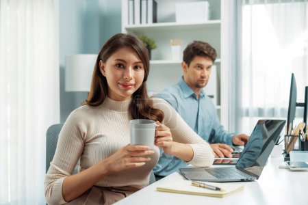 Photo for Smiling beautiful woman holding coffee cup to pose for looking at camera photo shooting portrait profiles business, working with smart coworker at modern office at morning on working desk. Postulate. - Royalty Free Image