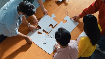 Photo for Top view of skilled business people gathering jigsaw piece together.Startup team with casual cloth standing at table while put jigsaw on table. Show unity, cooperation and team working. Convocation. - Royalty Free Image
