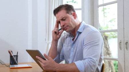 Geschäftsmann müht sich, das Arbeitsproblem von zu Hause aus mit dem Laptop zu lösen, sitzt zu Hause mit gestresstem und frustriertem Gesichtsausdruck auf seinem Schreibtisch und versucht, eine Lösung für das Problem zu finden. Synchronos