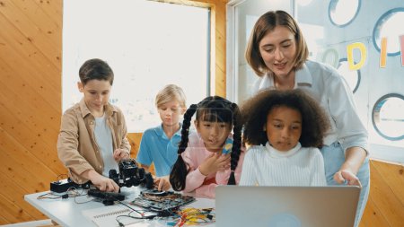Photo for Caucasian teacher praise student while looking at learner work or presentation. Group of diverse student looking at presentation and fixing motherboard at table with chips and wires placed. Erudition. - Royalty Free Image