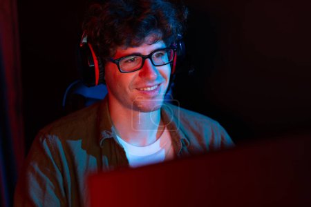 Lächelnde junge Gaming-Streamer-Team spielt mit Steuerknüppel auf Esport online auf PC-Kampfspiel, versuchen Sie, Konkurrenten bei der Strategieplanung für die nächste härtere an roten Neonbeleuchtung modernen Raum zu gewinnen. Gusher.