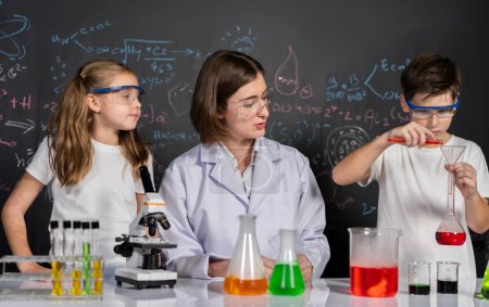 Photo for Teacher in support and watch student in laboratory they wear safety glasses, stand and experiment about science of chemistry in STEM class. Student funny do experiment with liquid in tube. Erudition. - Royalty Free Image