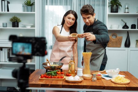 Couple chef influencers on cooking show presenting ingredient of spaghetti, meat, chilli, tomato, garlic and seasoning sauces homemade special recipe recording on camera on live channel. Postulate.