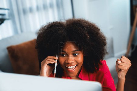Téléchargez les photos : Femme africaine parlant avec un collègue ou un ami au téléphone et regardant l'écran avec un visage heureux. Réalisation pour la promotion du poste de travail dans l'entreprise avec la bonne nouvelle de la vie. Tastemaker. - en image libre de droit
