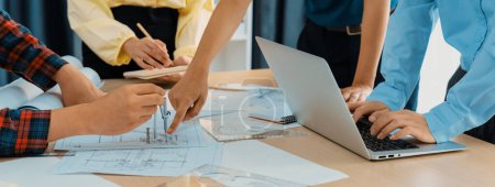 Photo for Skilled architect engineer team discuss about architectural project while project manager using laptop analysis data at meeting table with architectural document scatter around. Closeup. Delineation. - Royalty Free Image