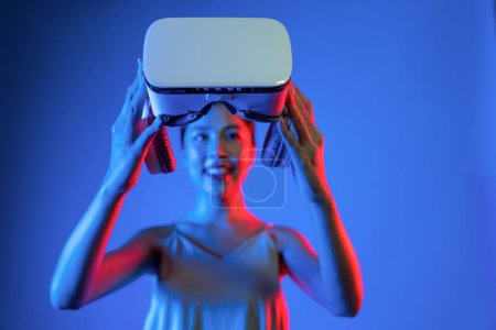 Photo for Smart female standing hit by neon light hold VR headset, gadget for connecting metaverse, future cyberspace community technology. Elegant woman carry and watch goggles with happy face. Hallucination. - Royalty Free Image
