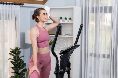 Photo for Athletic and sporty woman running on elliptical running machine during home body workout exercise session for fit physique and healthy sport lifestyle at home. Gaiety home exercise workout training. - Royalty Free Image
