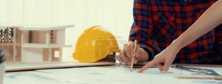 Photo for Cropped image of cooperative architect team decide and work together on meeting table with house model, safety helmet and architectural plan scatter around. Closeup. Focus on hand. Burgeoning. - Royalty Free Image