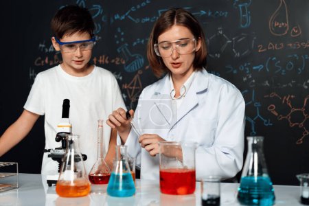 Photo for Teacher support schoolboy in laboratory. Schoolboy and teacher stand and experiment about science of chemistry in STEM class using liquid in glass container. Instructor mixing solution. Erudition. - Royalty Free Image