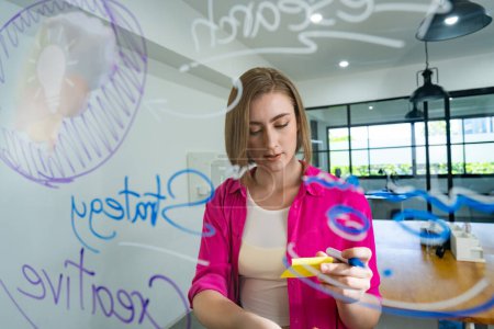 Photo for Closeup of attractive smart caucasian businesswoman brainstorms and planing marketing idea by using mind map and colorful sticker on glass board. Creative start up business concept. Immaculate. - Royalty Free Image