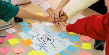 Photo for A group of business people putting their hands together at meeting room on table with mind map scatter around. Startup group showing unity teamwork and friendship. Close up. Focus on hand. Variegated. - Royalty Free Image