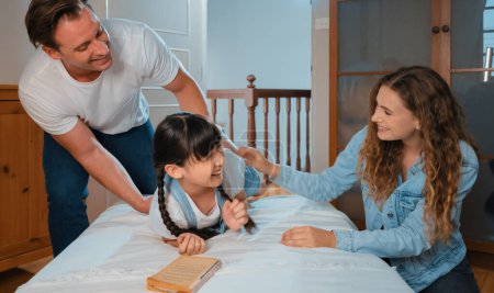 Happy modern family wakes up their little girl on the weekend with playful tickle expressing their love and affection for their young daughter, laughing and smiling together. Synchronos