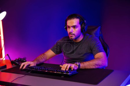 Photo for Smart gaming streamer concentrating gaming players trying to pass the level at mission completed, using headset and mic for communicate others on streaming live at neon lighting studio room. Surmise. - Royalty Free Image