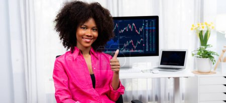 Photo for Analytical young African American businesswoman, a specialist in successful stock exchange trading, against dynamic data graph displaying marketing trend analysis on screen. Tastemaker. - Royalty Free Image