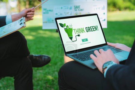 Foto de Grupo de empresarios asiáticos que planean un plan de desarrollo respetuoso con el medio ambiente en la pantalla del portátil y un proyecto de tecnología sostenible para un futuro más verde, eco oficina al aire libre en el parque natural. Gyre. - Imagen libre de derechos