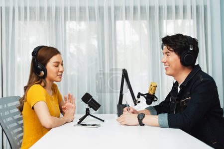 Smiling radio influencer host wearing headphone interviewing woman speaker sharing information to listeners on social media online website live streaming channel at morning at studio record. Infobahn.