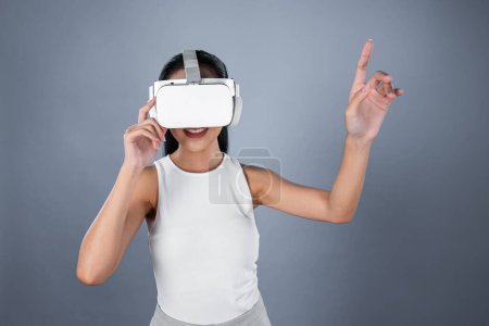 Photo for Smart female standing with gray background wearing VR headset connecting metaverse, futuristic cyberspace community technology. Elegant woman excited seeing generated virtual scenery. Hallucination. - Royalty Free Image