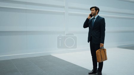 Skilled manager using phone call to contact colleague about project. Handsome male leader calling his business team to report and discuss about sales while standing at white background. Exultant.
