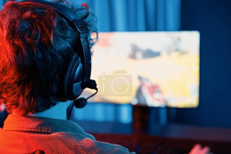 Host-Kanal von jungen Gaming-Streamer, Team-Gamer, die Battle Game Shooting mit Multiplayer auf Kriegsschiff auf dem PC-Bildschirm mit Rückseite Bild, trägt Headset mit Mikrofon im digitalen Neon-Raum. Gusher.