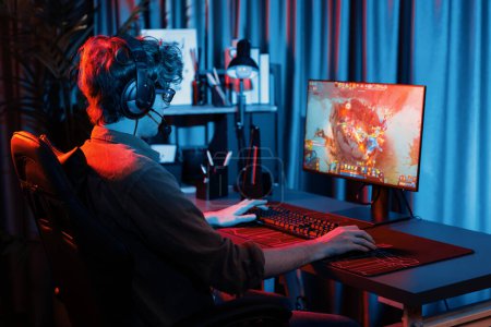 Host-Kanal von jungen Gaming-Streamer spielen Kampf Moba in der Schlacht Arena Spiel mit Multiplay-Team, trägt Kopfhörer auf dem PC-Monitor mit Rückseite Bild in Neon-Digitallicht modernen Raum. Gusher.