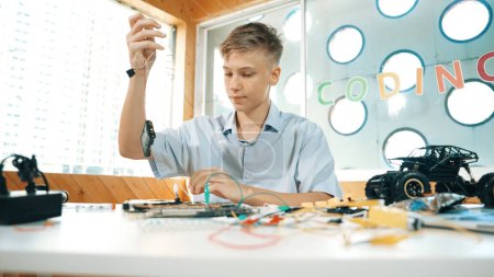 Smart happy boy inspizieren oder lernen, elektronische Werkzeuge zu verwenden, um Auto-Modell zu reparieren. Highschool-Schüler lernen im MINT-Unterricht über elektrische Geräte zur Reparatur von Robotermaschinen. Erbauung.
