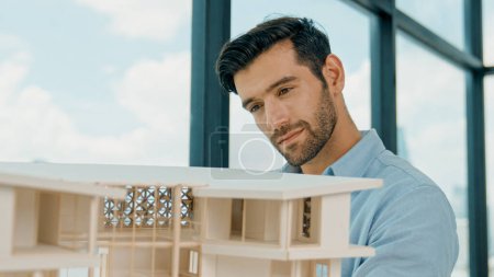 Photo for Skilled smiling caucasian engineer turns house model left and right to check mistake point. Professional manager inspect, checking, looking at architectural model. Design concept. Tracery - Royalty Free Image