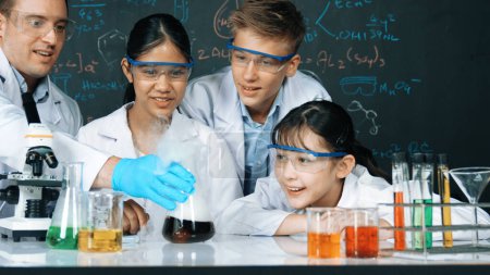 Mädchen beim Experimentieren an der Tafel mit Chemie-Theorie im MINT-Unterricht. Lehrer und eine Gruppe von High-School-Schülern mit gemischten Rassen machen gemeinsam naturwissenschaftliche Aktivitäten. Erbauung.