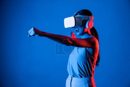 Foto de Mujer inteligente de pie con auriculares VR que conectan metaverse, tecnología futura de la comunidad del ciberespacio. Elegante mujer que usa el juego de lucha de personajes de jugador de control de postura de perforación. Alucinaciones. - Imagen libre de derechos
