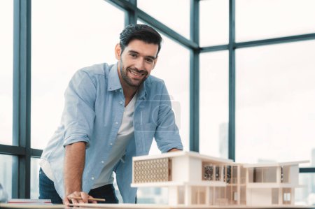 Photo for Smiling caucasian architect engineer looking at camera while standing with house model. Smart interior designer standing while holding pencil. Project plan, civil engineering, worker. Tracery. - Royalty Free Image