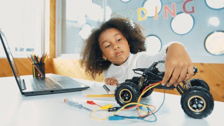 Photo for Smart african girl build robotic car while using wires while using laptop setting or writing prompt code. Skilled female student working on computer in STEM technology online classroom. Erudition. - Royalty Free Image