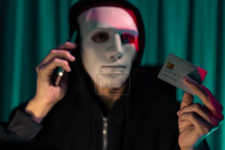 Téléchargez les photos : Masque anonyme criminel blanc appelant le propriétaire de la carte de crédit pour menacer de rançon avec des informations de confidentialité toute la base de données, ce qui rend le cryptage de mot de passe par piratage de programmation essayant de rendre non sécurisé. Pécuniaire. - en image libre de droit