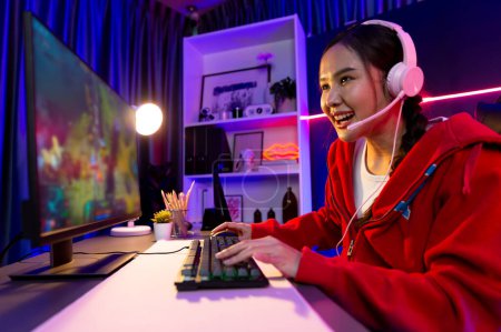 Anfitrión canal de la joven hermosa asiática juego streamer jugando Moba lucha en batalla juego de arena en la pantalla de PC con multiplays, usando auriculares pastel en neón luz digital habitación moderna. Estratagema.