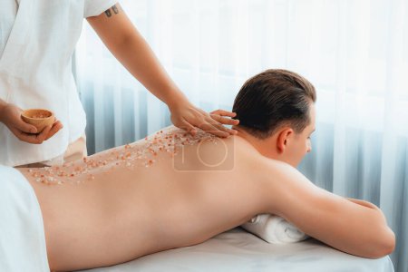 Photo for Blissful man customer having exfoliation treatment in luxury spa salon with warmth candle light ambient. Salt scrub beauty treatment in health spa body scrub. Quiescent - Royalty Free Image