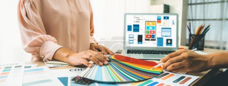 Photo for Cropped image of interior designer chooses color from color swatches while laptop displayed UI and UX designs for mobiles app and website. Creative design and business concept. Variegated. - Royalty Free Image