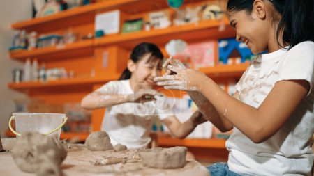 Photo for Happy multicultural girl and friend put the clay on the each other muddy shirt at art lesson. Diverse highschool student playing with clay at pottery workshop. Creative activity concept. Edification. - Royalty Free Image